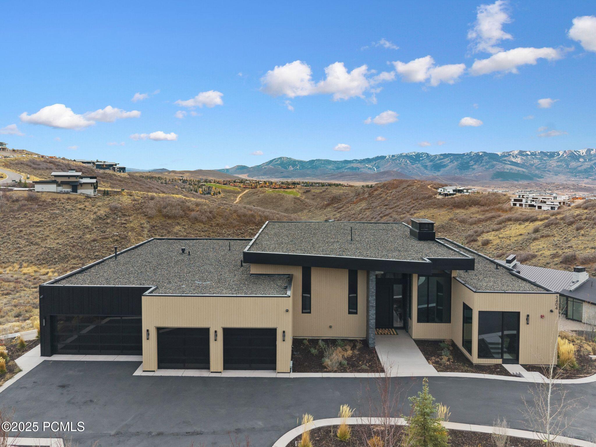 Modern tan-and-black hillside home with multiple garage doors and mountain views.