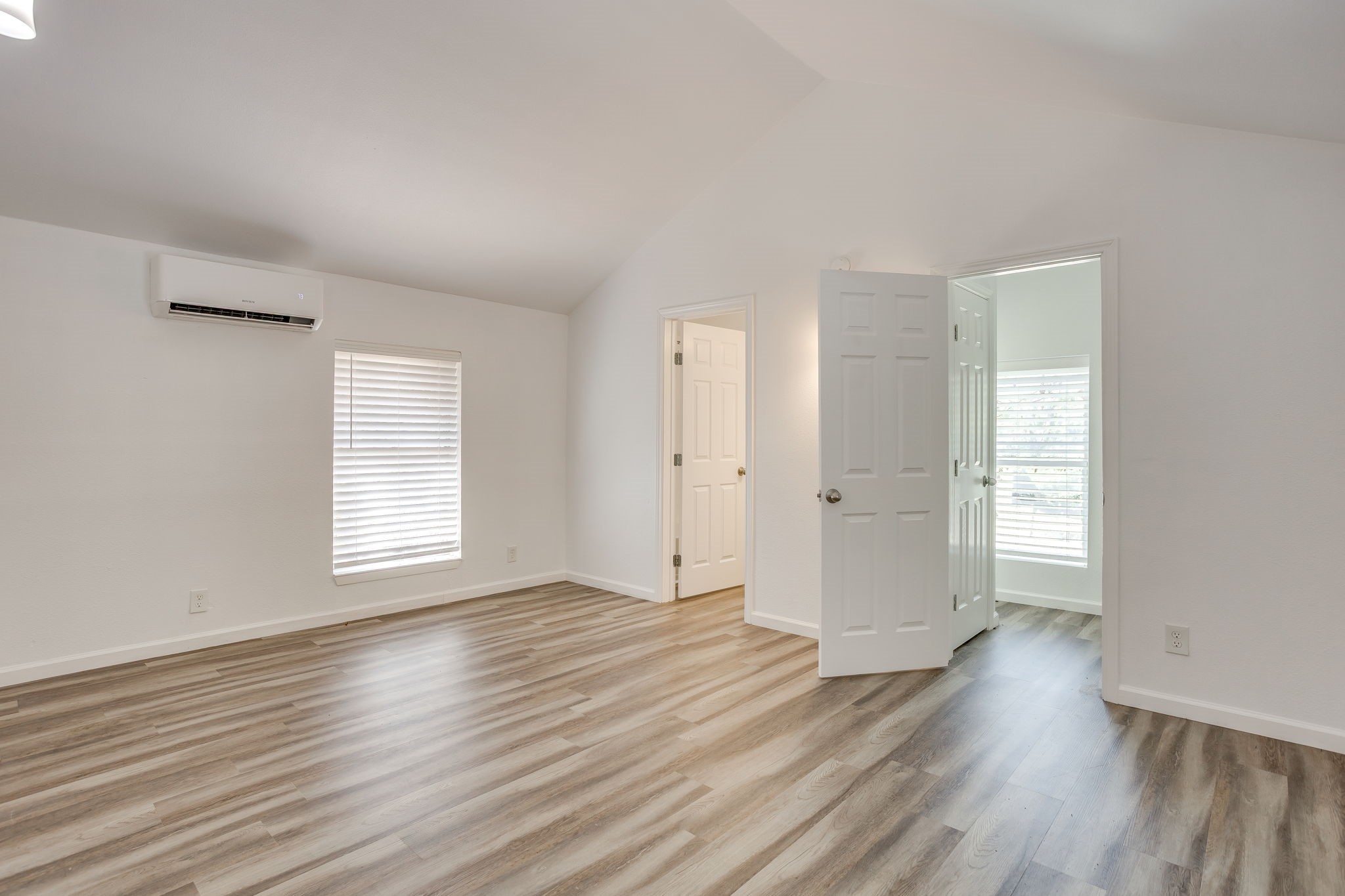 Vacant room with wood-look flooring, a wall-mounted mini-split, and open doorways.