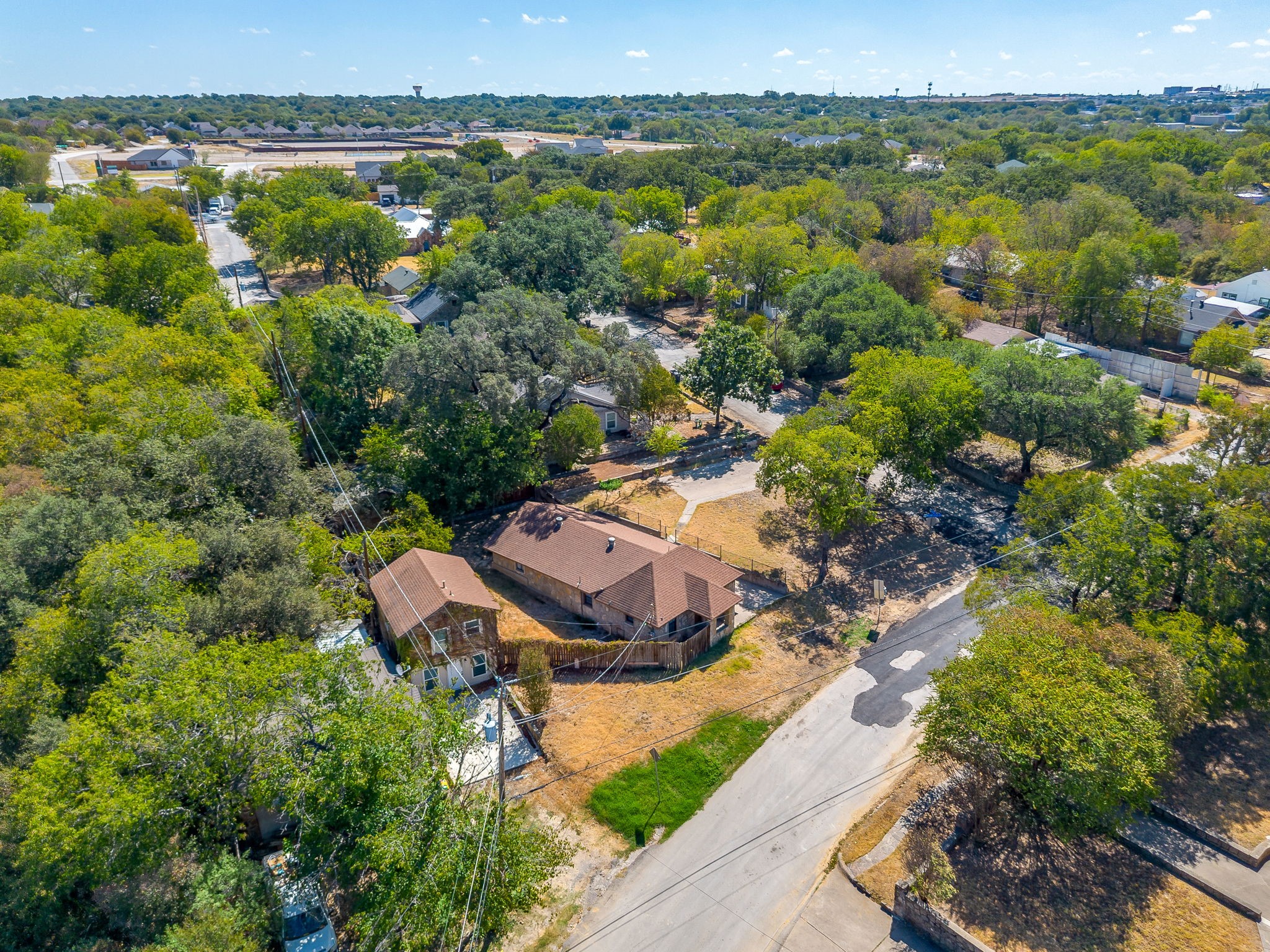 Aerial view of a brick home with a fenced yard, mature trees, and a road nearby.