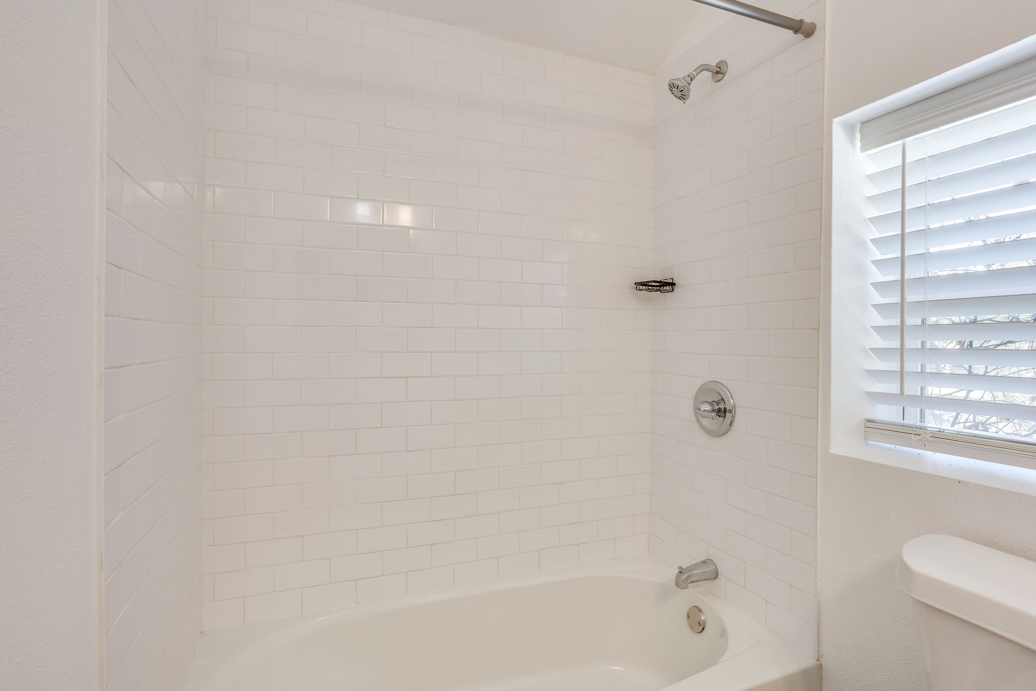 Bathroom with a white subway-tile tub surround, chrome shower fixtures, and a window with blinds.