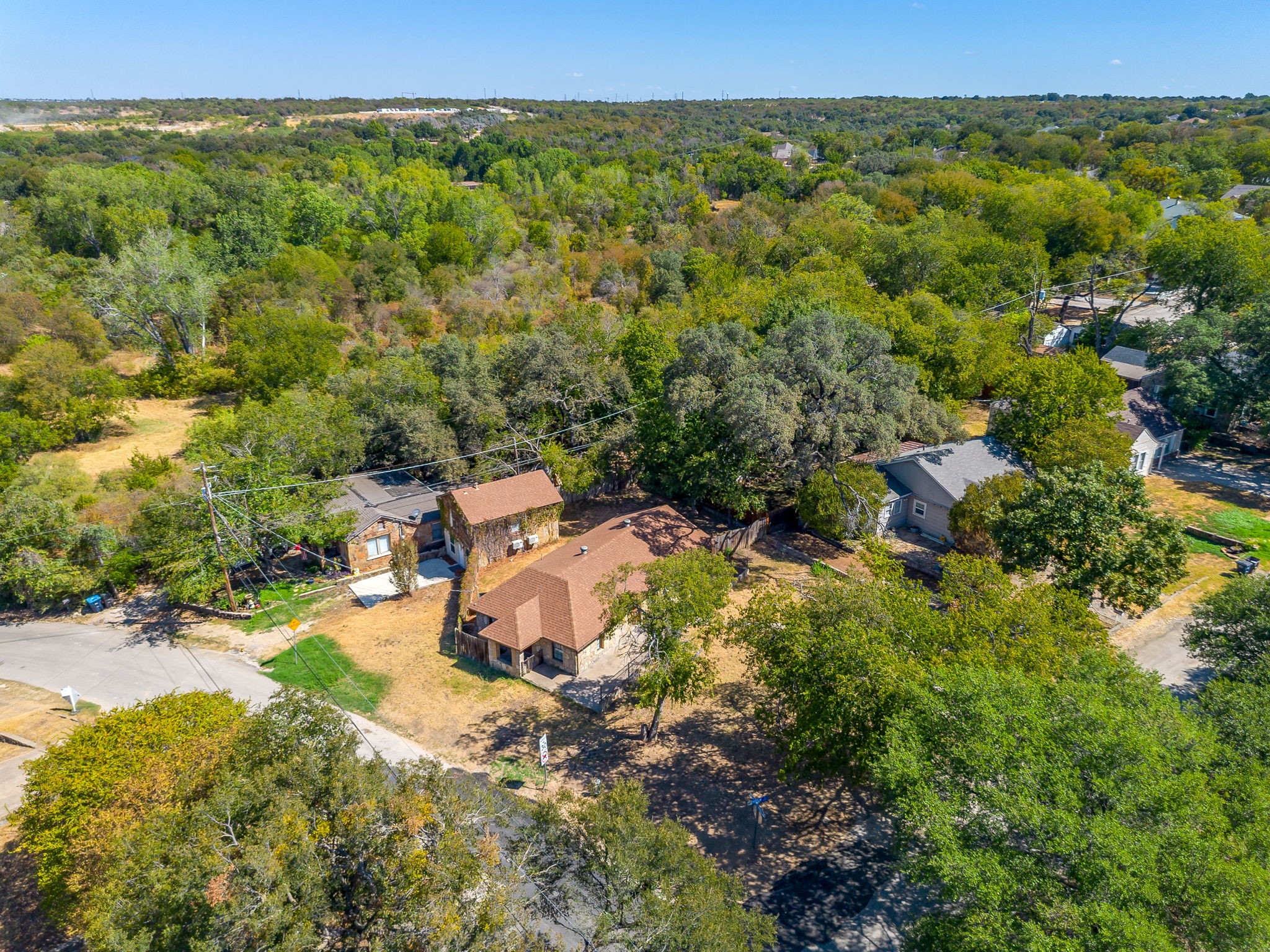 Aerial view of a house with a dry yard surrounded by mature trees and neighboring homes.