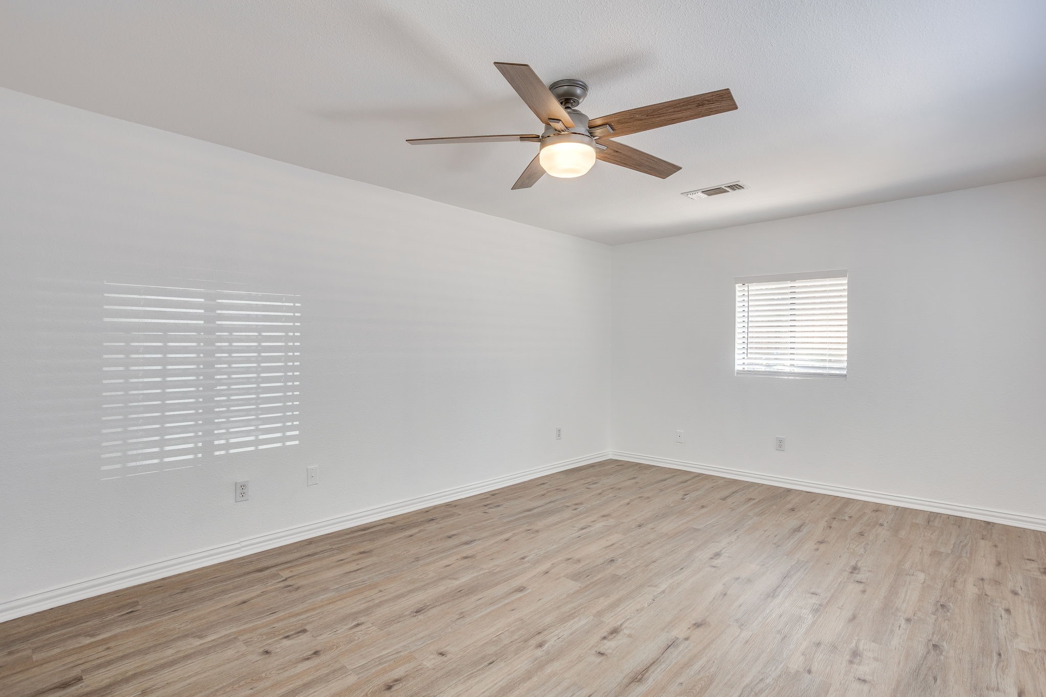 Empty room with light wood-look flooring, a ceiling fan, and a window with white blinds.