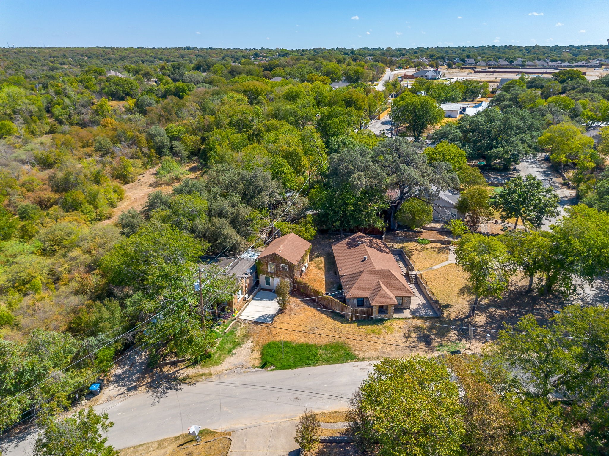 Aerial view of two houses amid trees, with open ground and a road along the property.