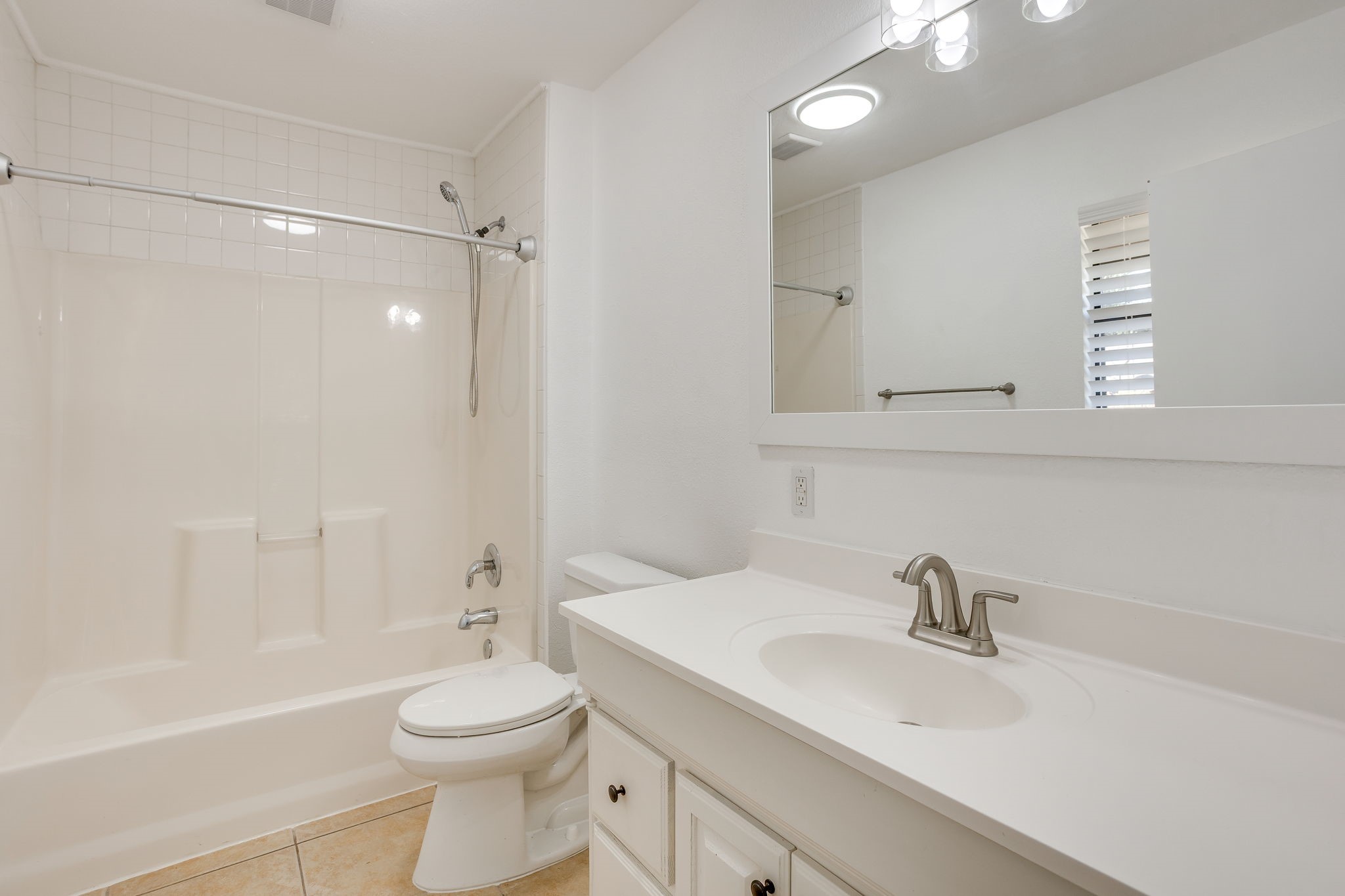 Bathroom with a white tub and shower, toilet, and vanity beneath a large mirror.