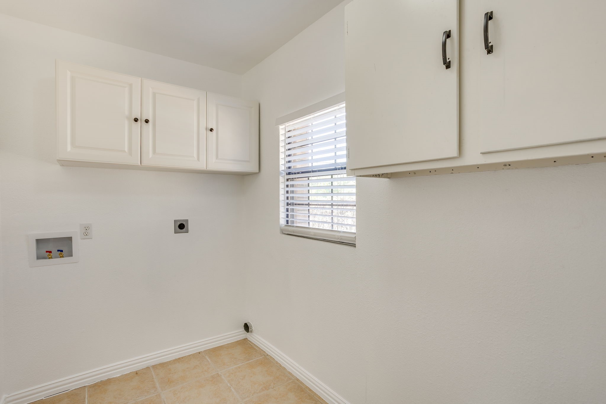 Empty laundry room with white cabinets, washer and dryer hookups, and a window with blinds.