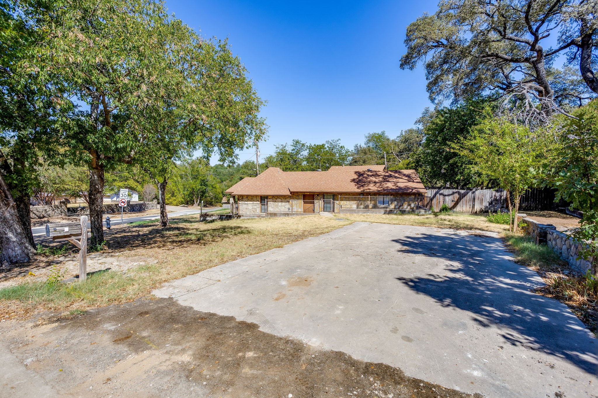 Single-story home with a covered porch and broad concrete driveway beneath mature trees.
