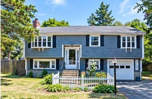 Blue split-level house with white trim, front steps, picket fence, and attached garage.