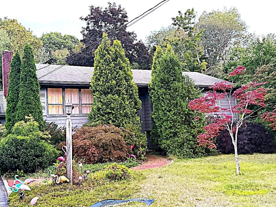 Gray single-story home partly screened by evergreens, with a curved brick walkway and landscaped front garden.