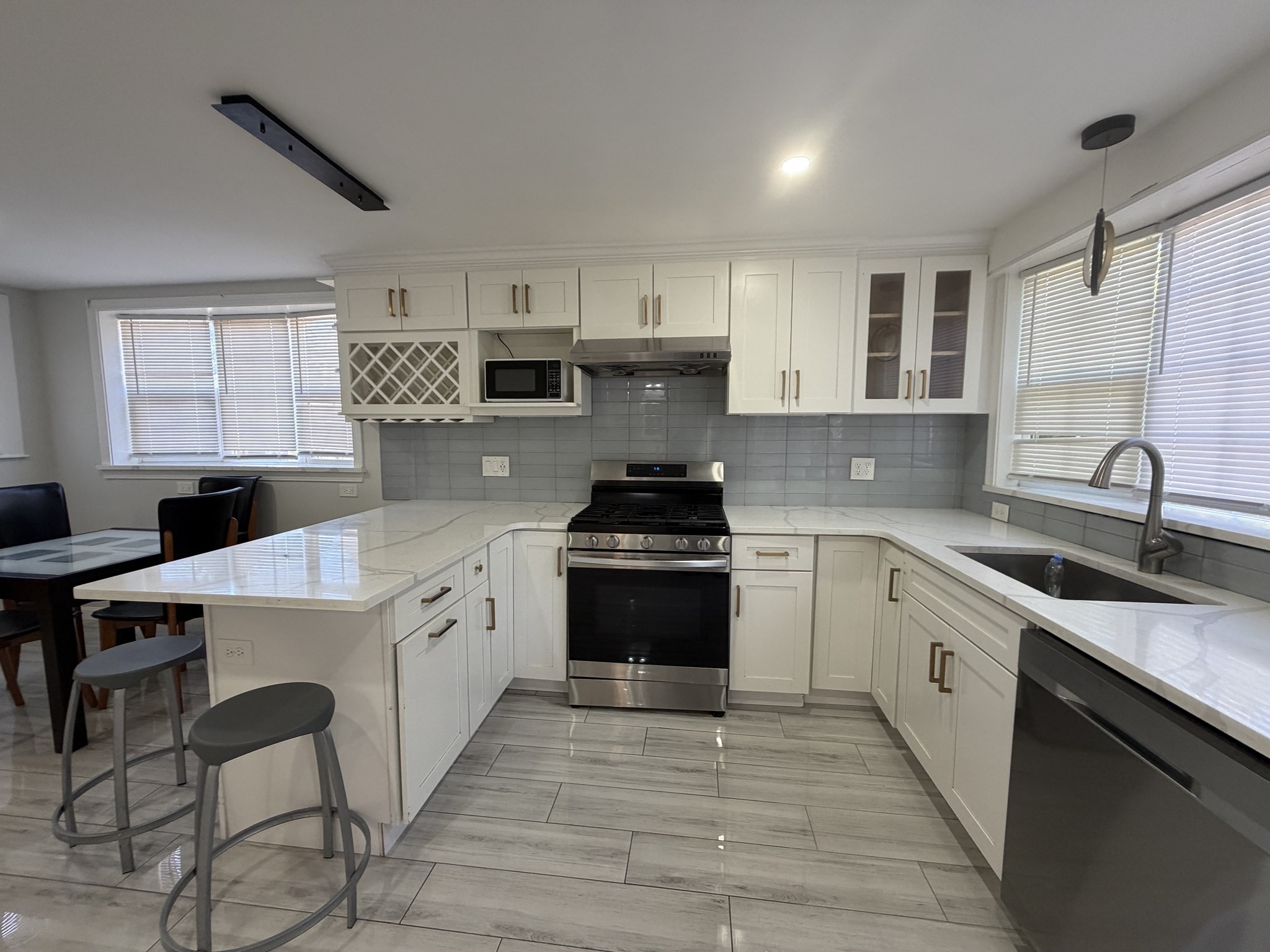 Renovated kitchen with white cabinets, gray tile backsplash, stainless range, and breakfast bar with stools.