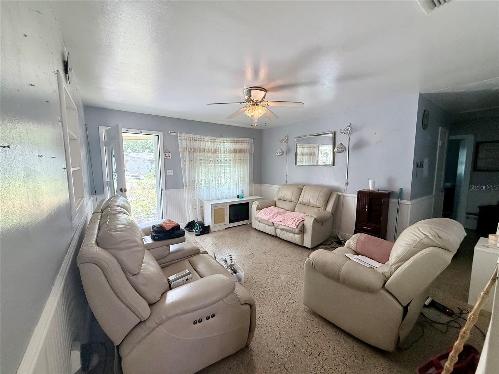 Living room with beige leather seating, ceiling fan, and open door to the outside.