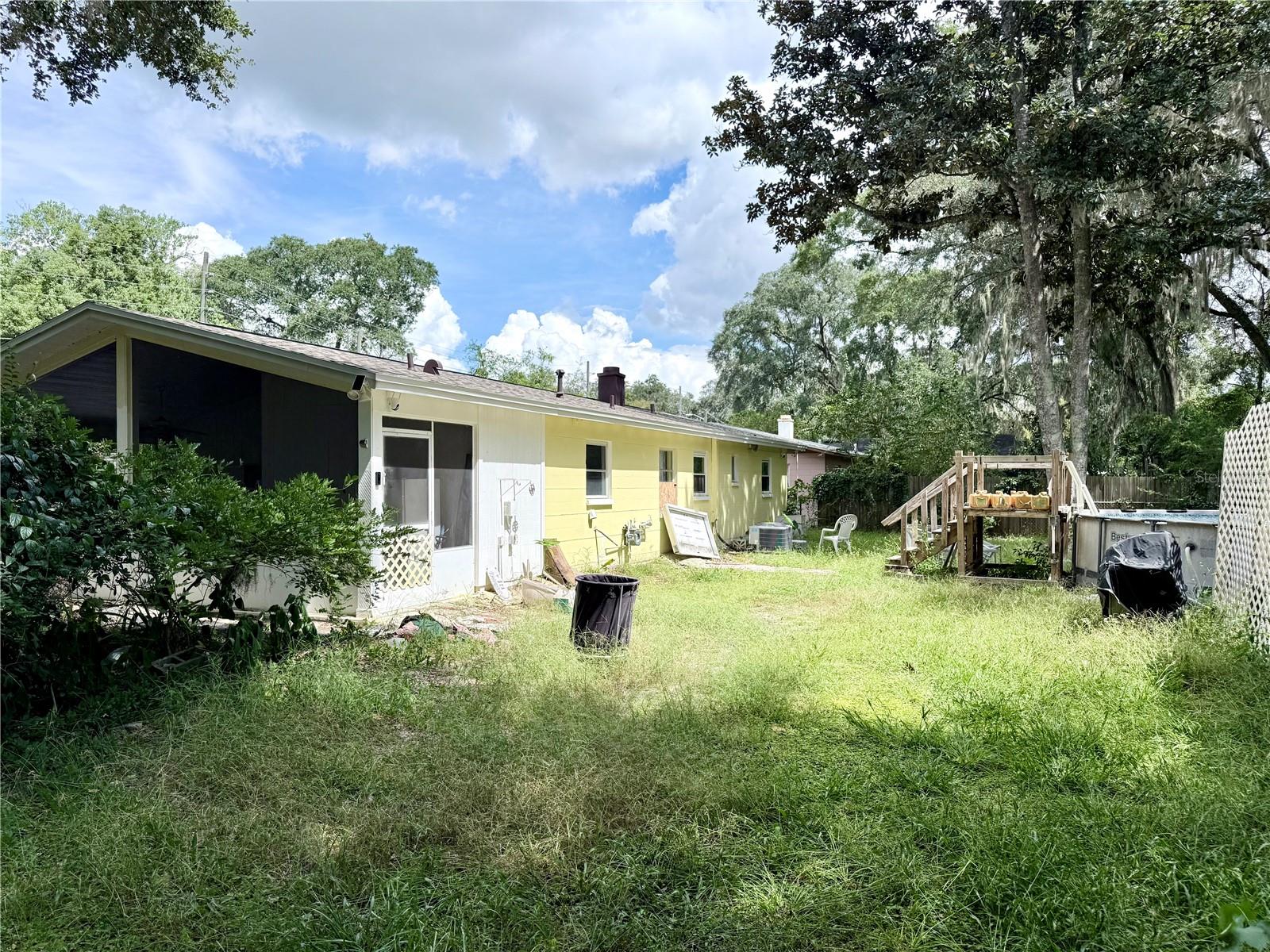 Yellow single-story house with a screened porch and grassy backyard, above-ground pool, and wooden deck.