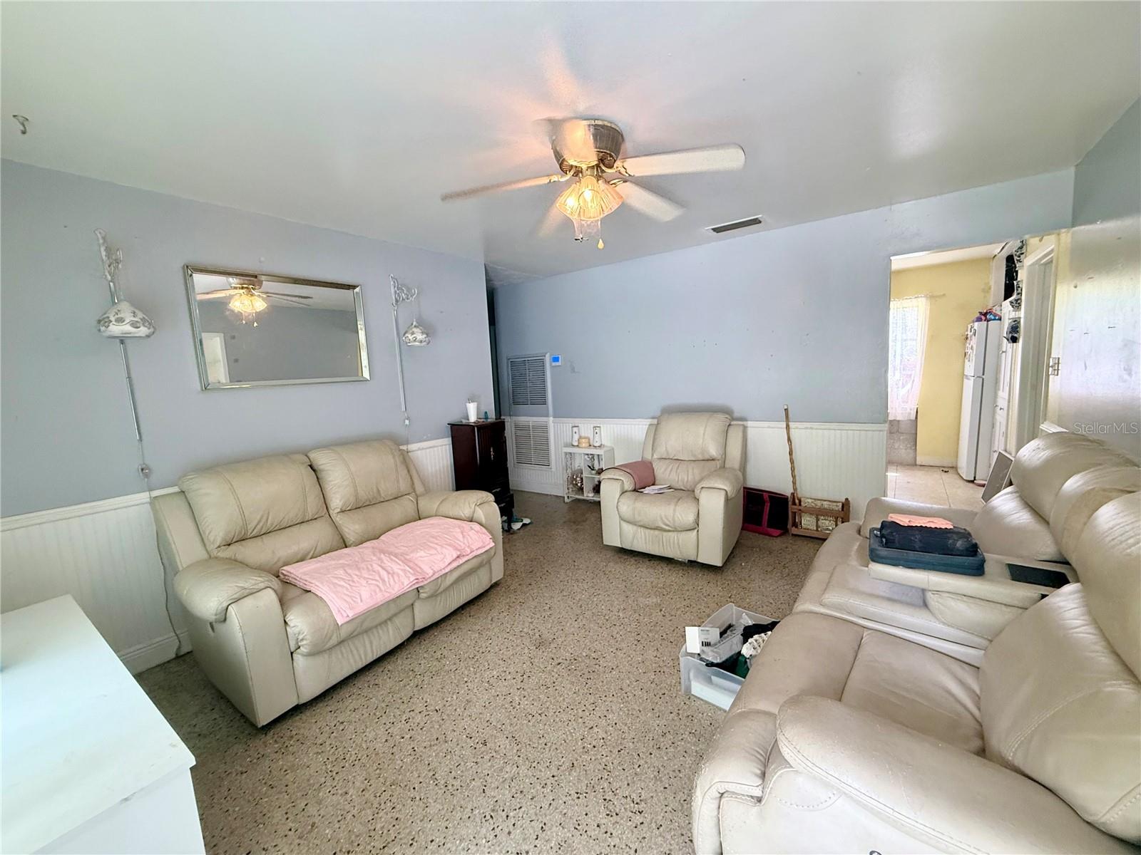 Living room with cream leather seating, gray walls, white wainscoting, and a ceiling fan.