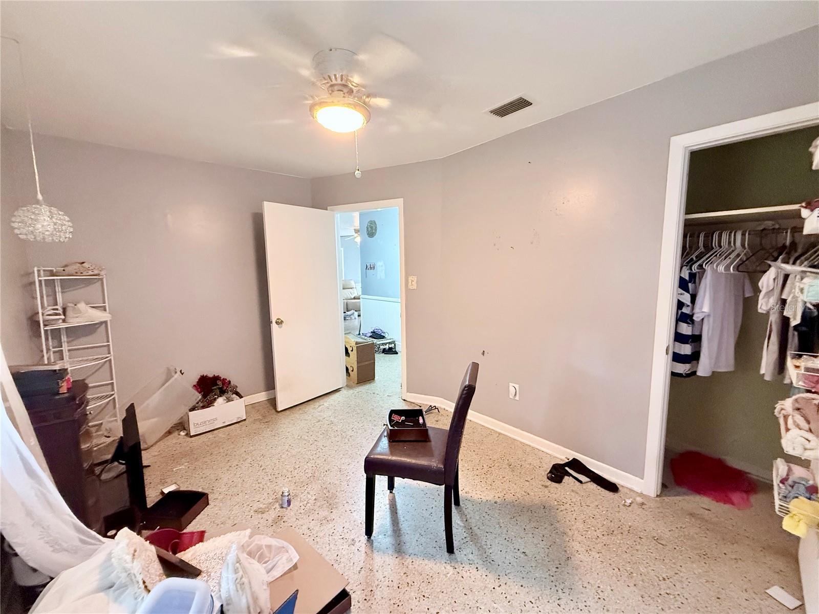 Bedroom with gray walls, a ceiling fan light, and an open closet filled with clothes.