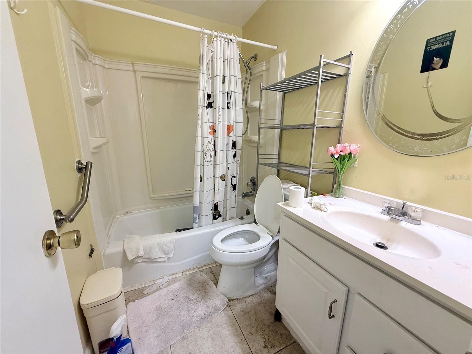 Bathroom with a tub-shower, patterned curtain, toilet, and long vanity.