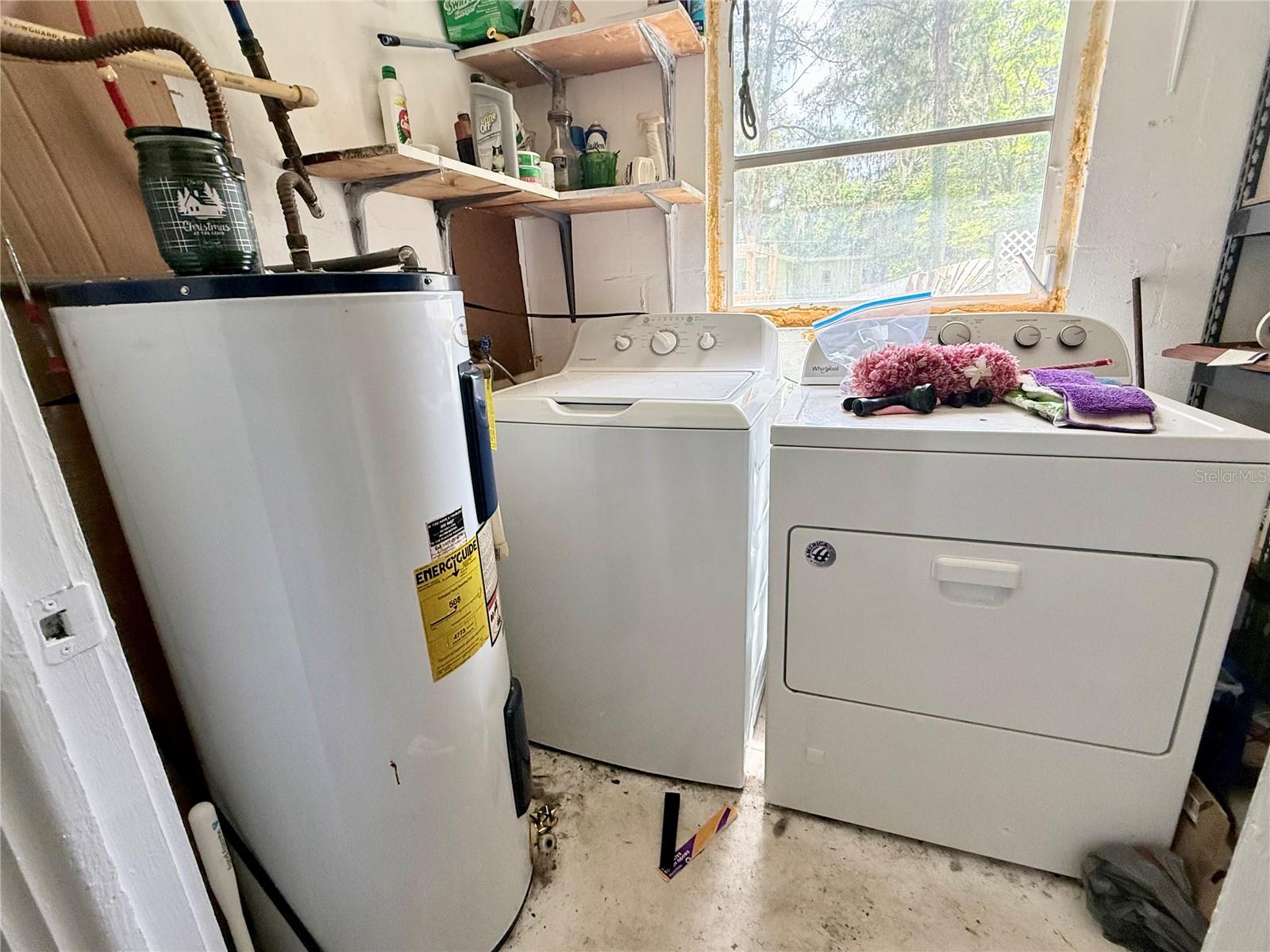 Laundry room with a washer, dryer, water heater, and open shelves beneath a large window.