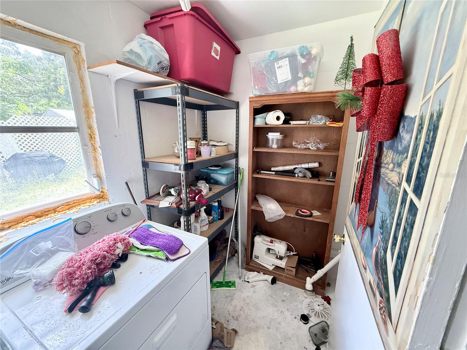Laundry room with a washer, crowded storage shelves, and a window.
