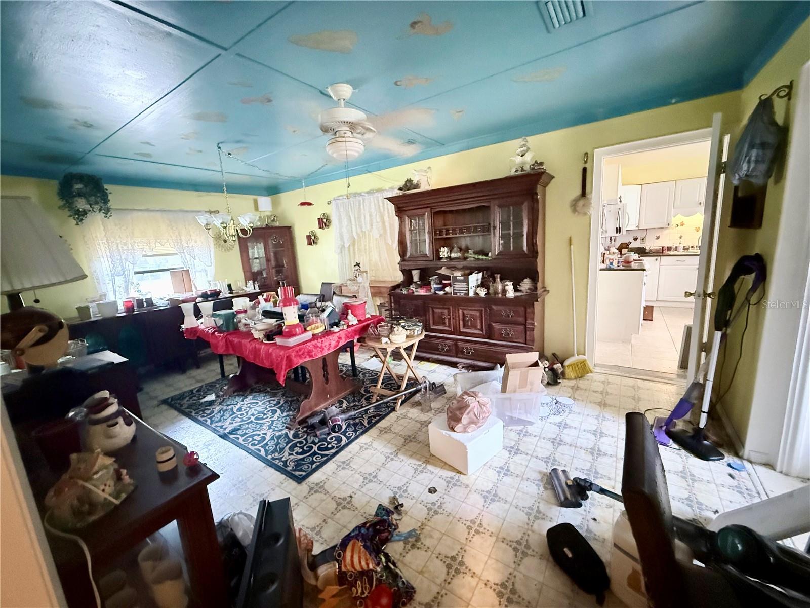Cluttered dining room with a dark wood china cabinet and vivid blue ceiling.