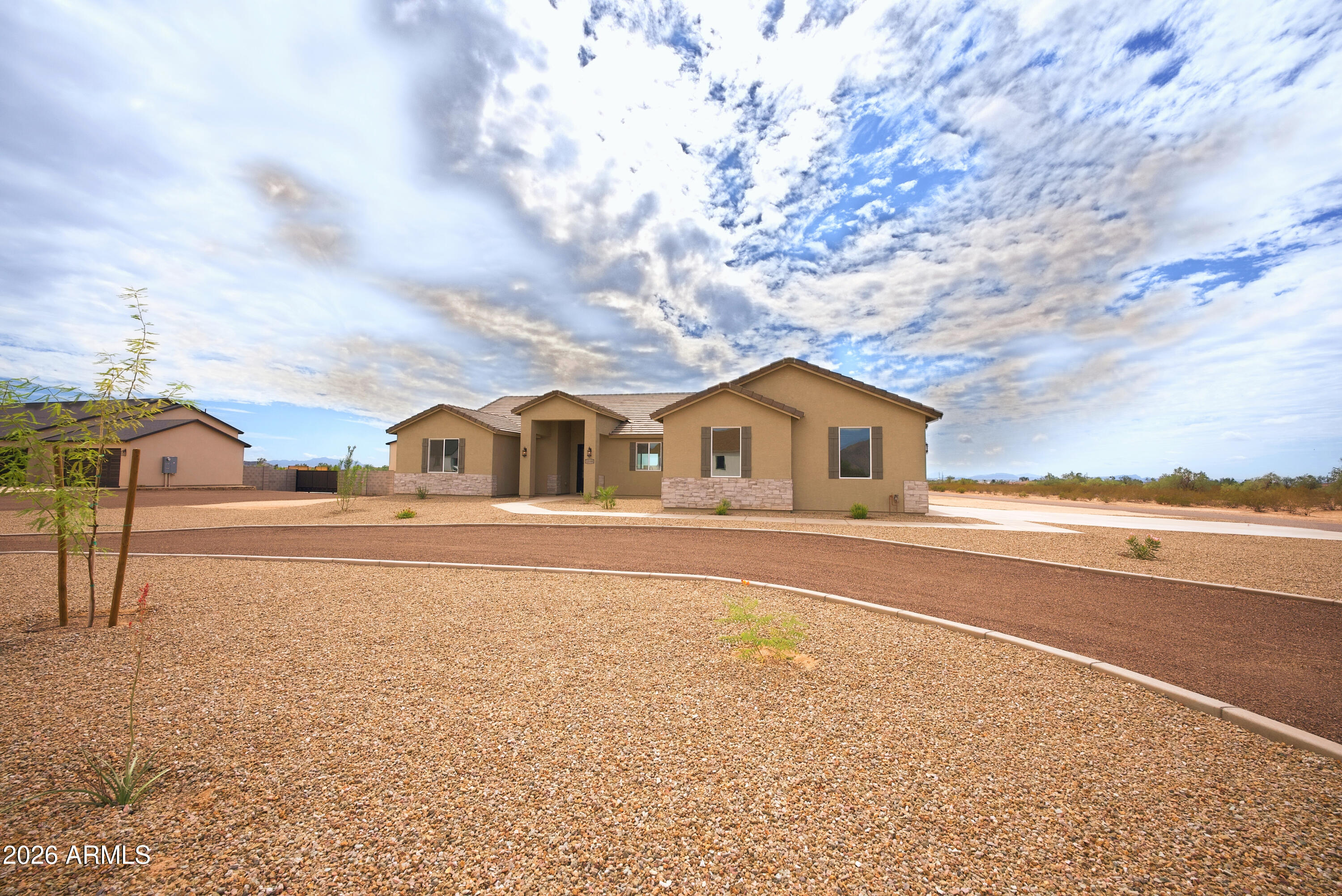 Single-story tan stucco house with stone accents, a covered entry, and a broad gravel yard.