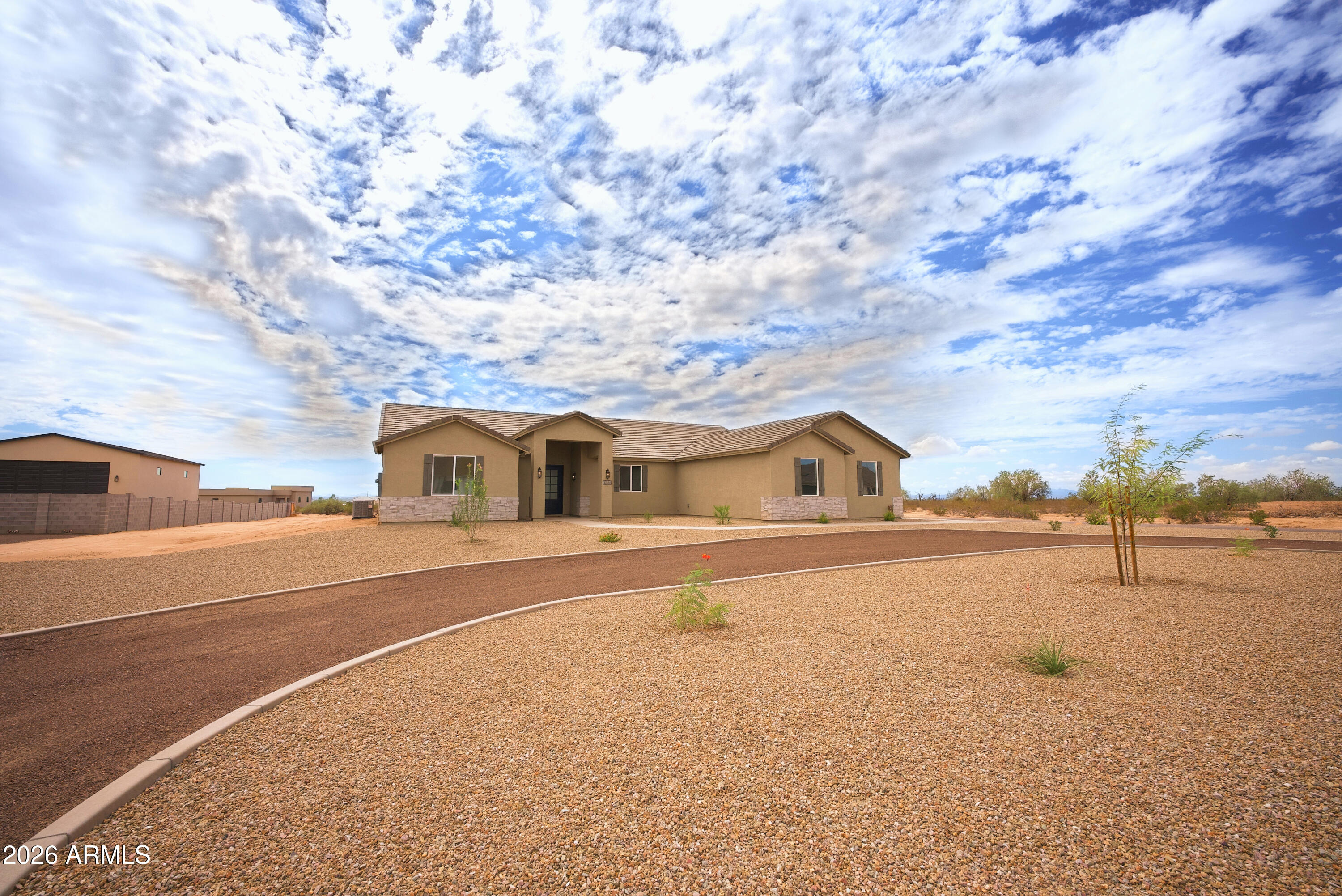 Single-story tan home with a covered entry and broad gravel desert landscaping.