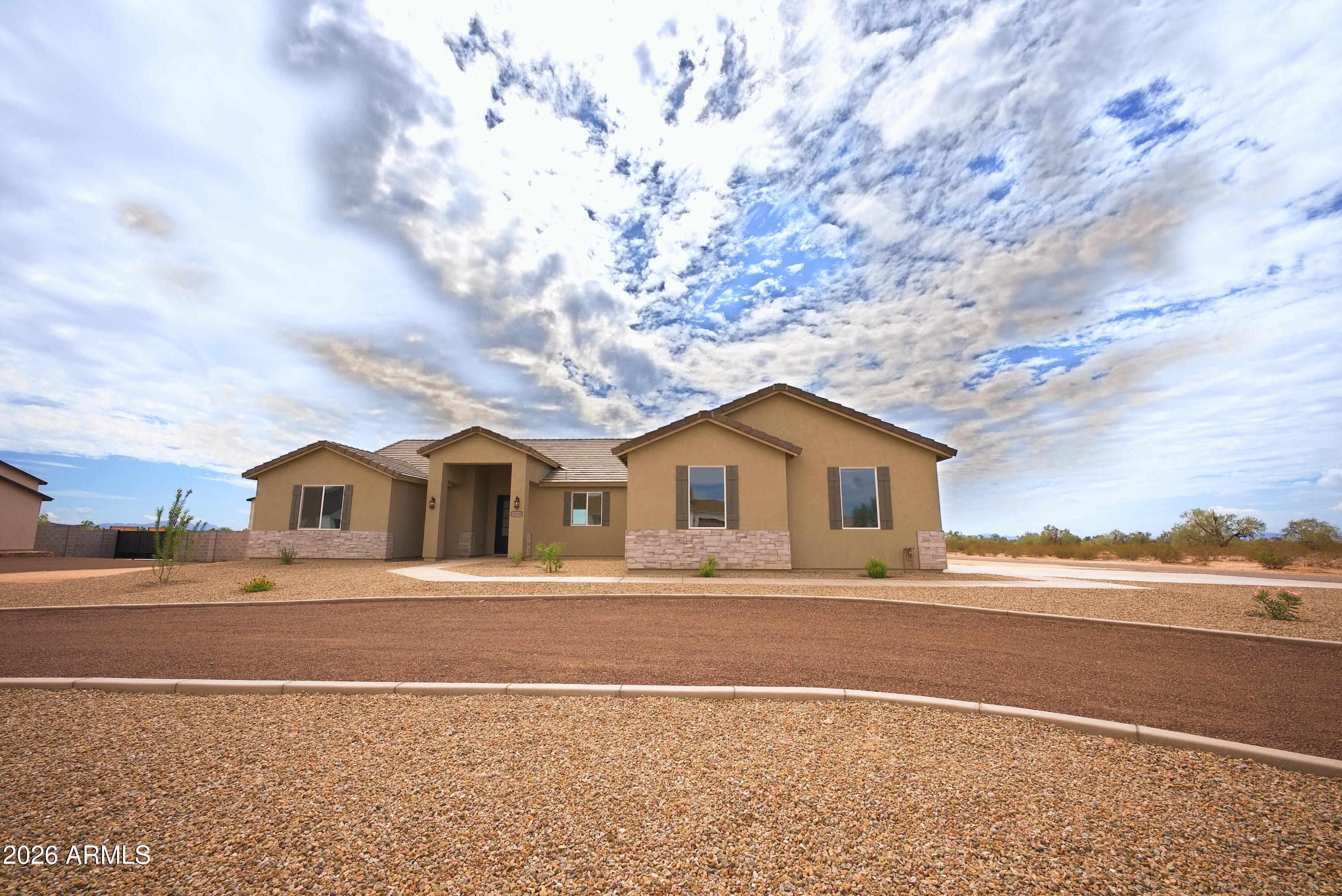 Single-story tan home with stone accents, a covered entry, and gravel landscaping.