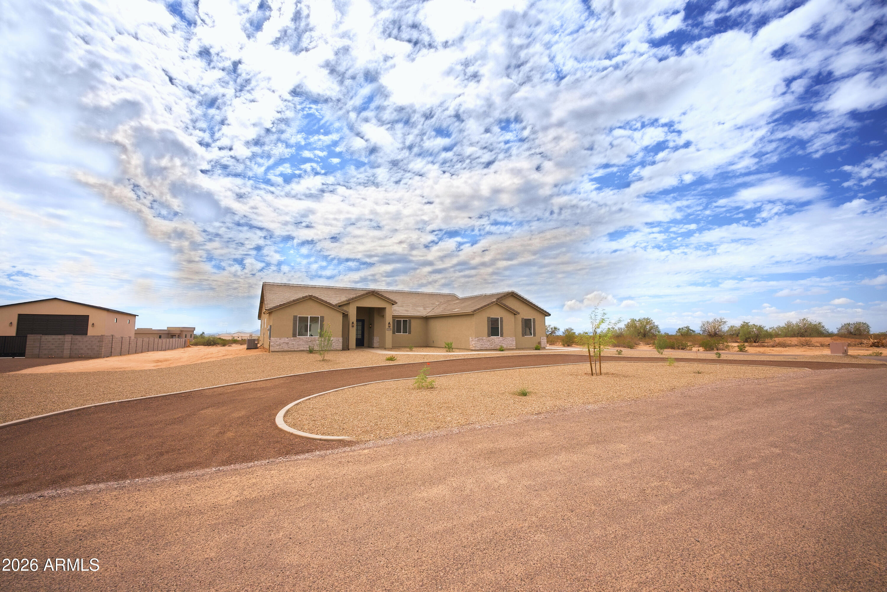 Single-story tan stucco home with a curved driveway and gravel desert landscaping.