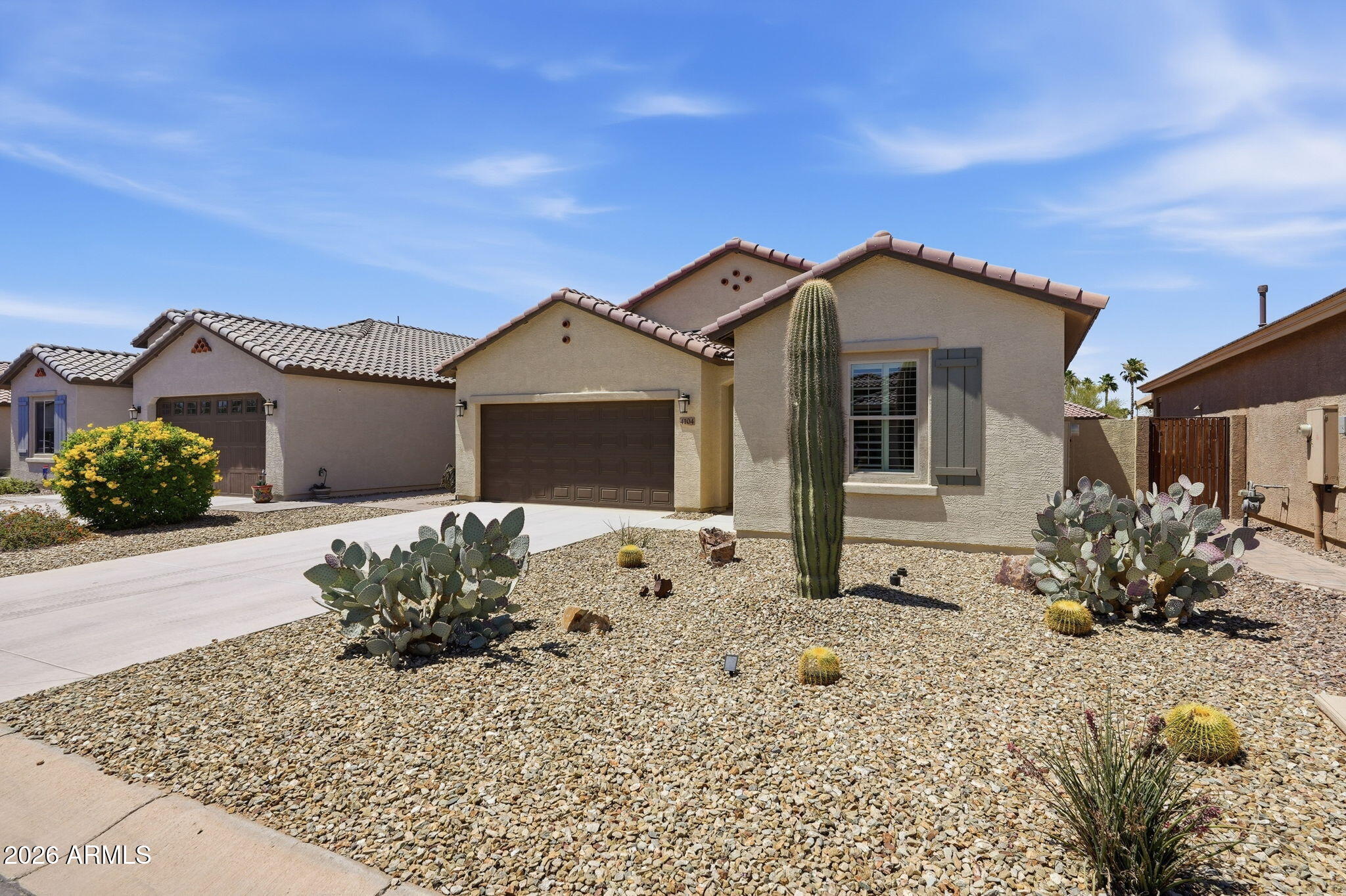 Single-story beige stucco home with a brown garage door and desert landscaping with cacti.