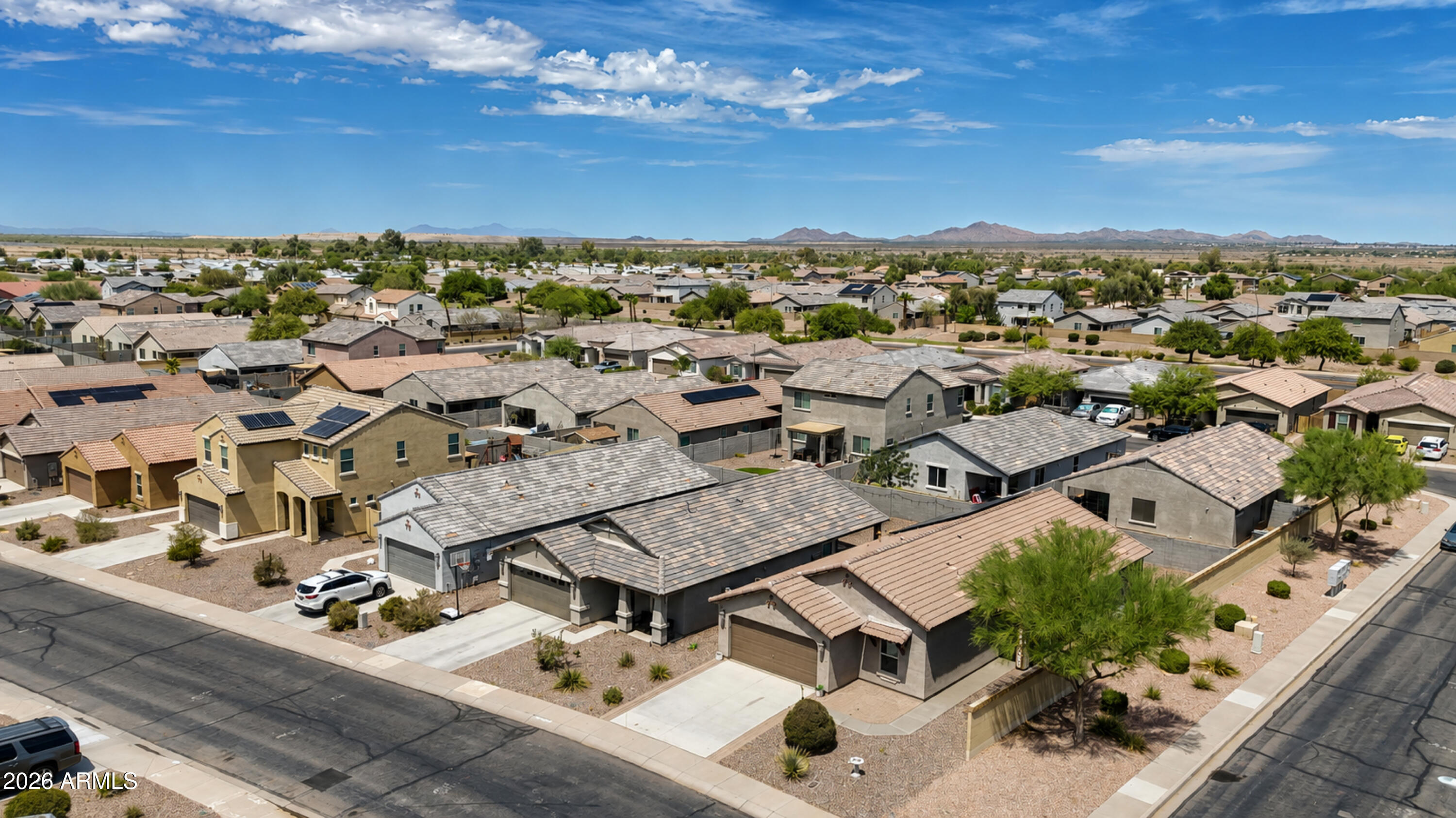 Aerial view of a corner-lot home with a tan tile roof and desert landscaping, with distant mountains.