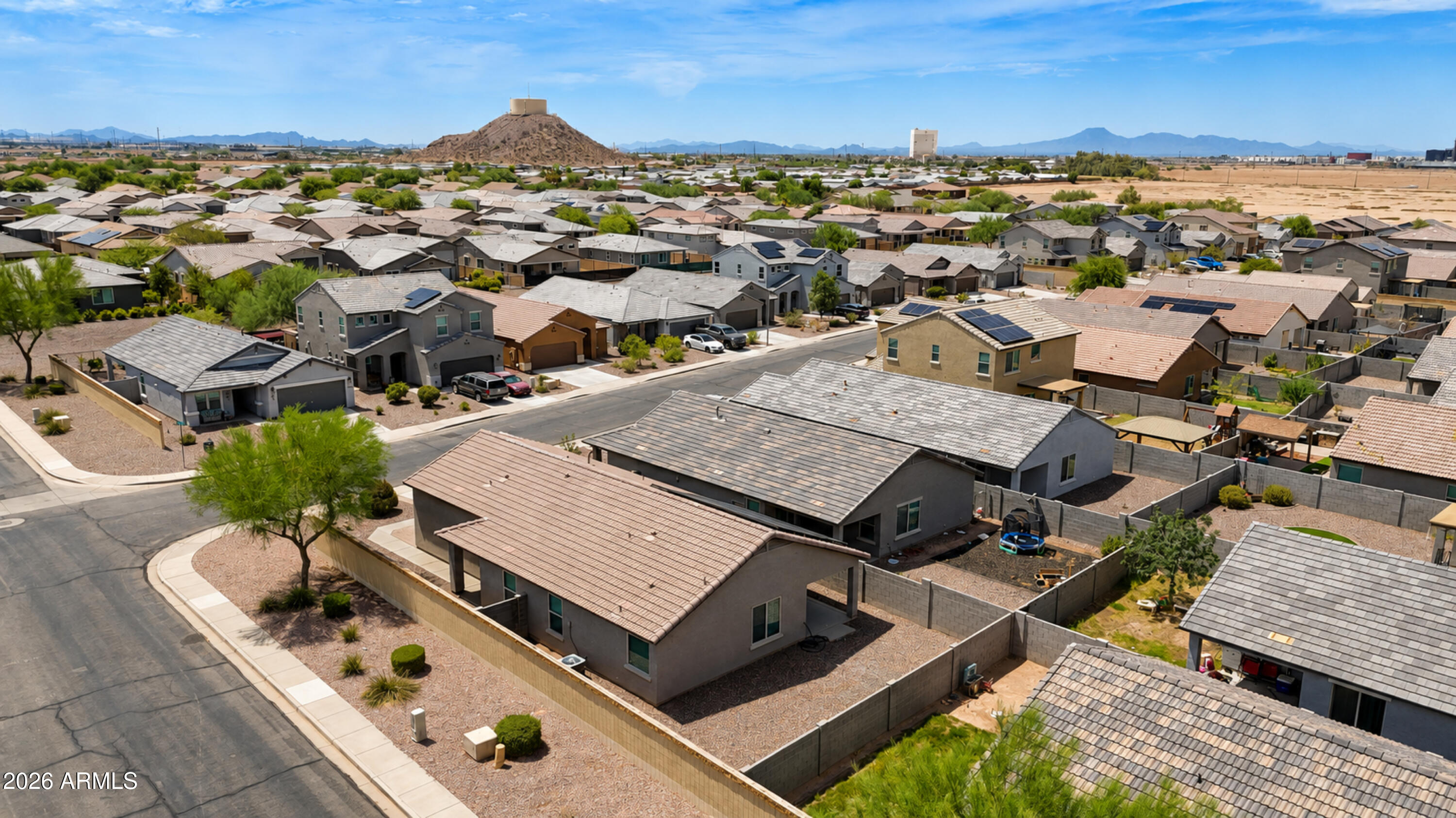 Aerial view of a desert neighborhood, with homes, a rocky hill, and distant mountains.