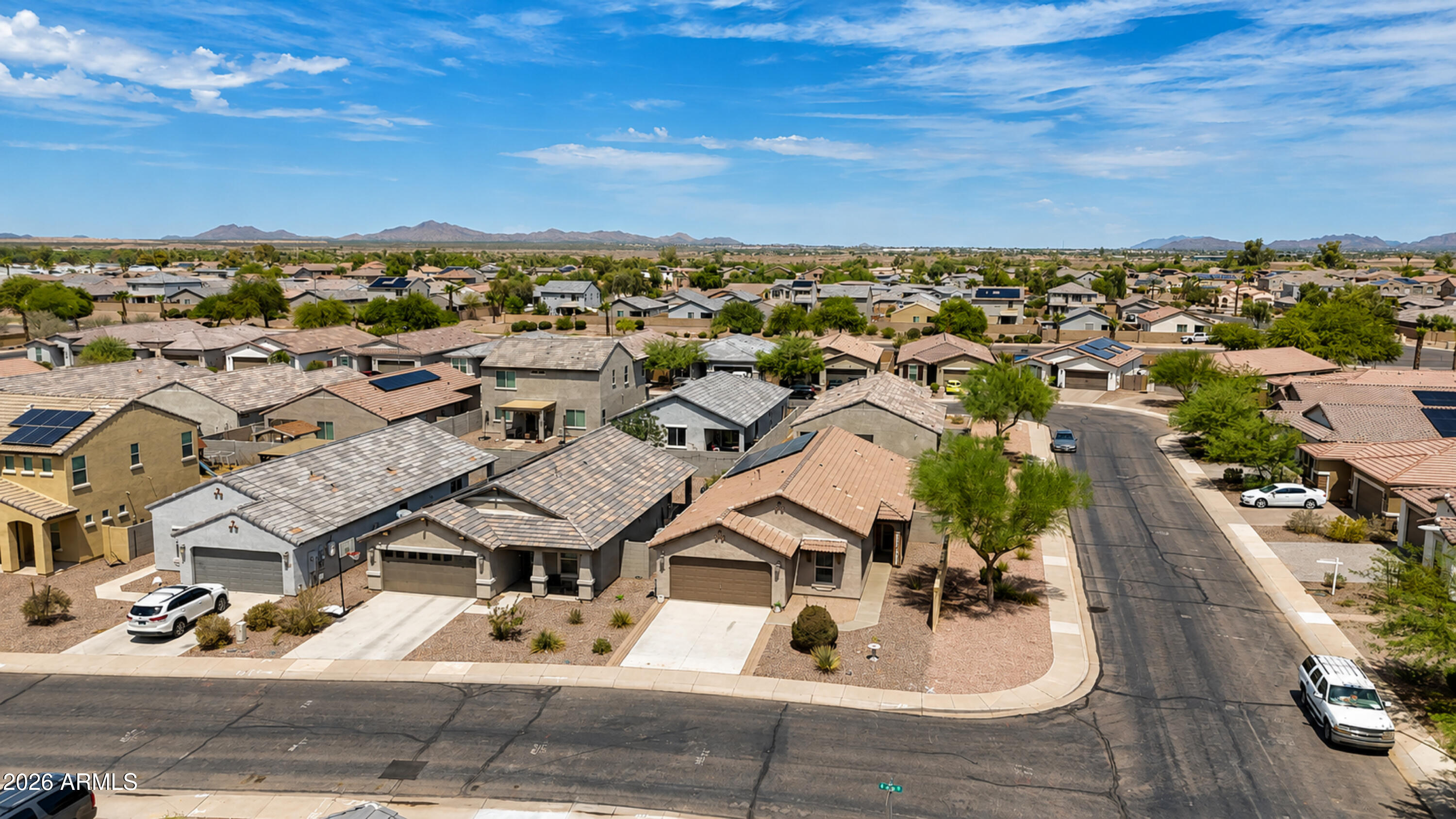Aerial view over stucco homes and desert landscaping, with mountains on the horizon.
