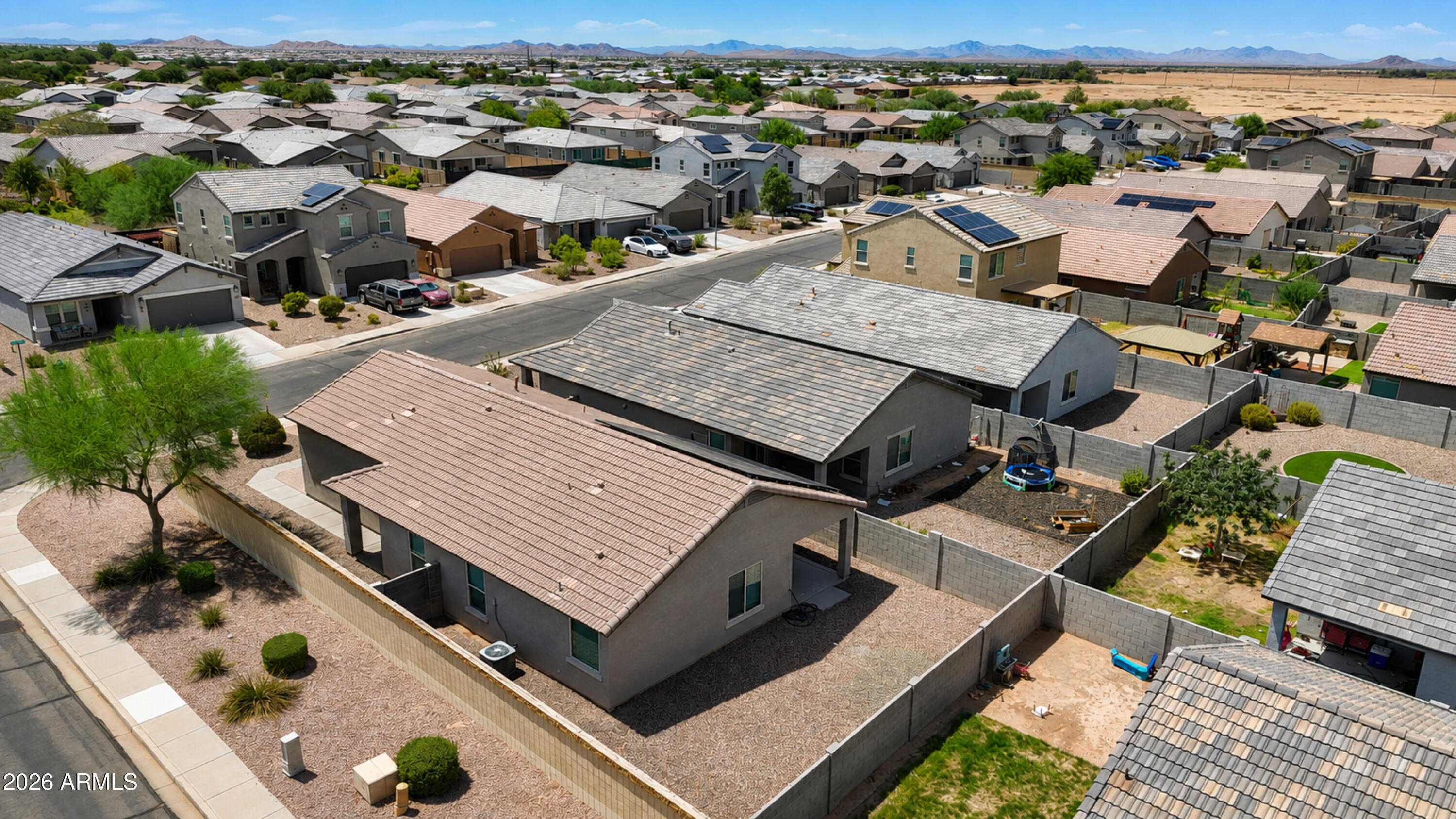 Aerial view of a single-story home with a fenced gravel yard and solar panels, with mountains in the distance.