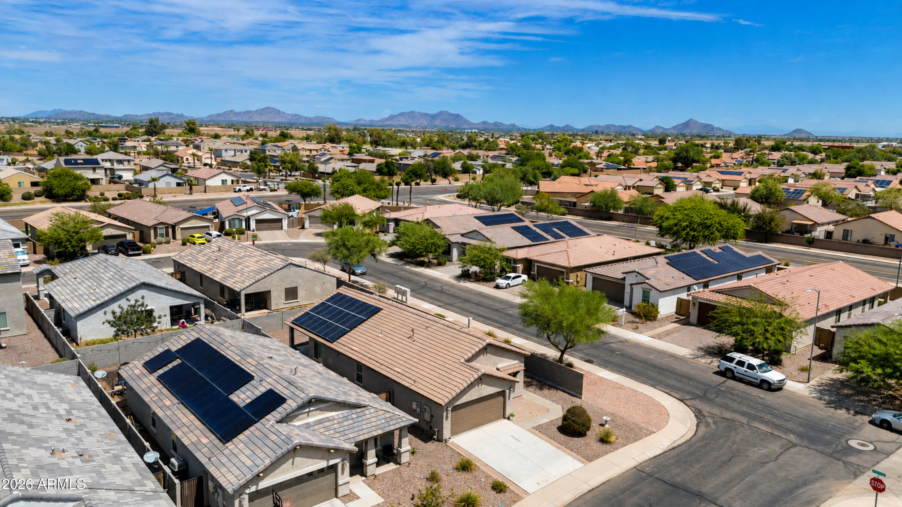 Aerial neighborhood view with solar-paneled roofs, desert landscaping, and mountains on the horizon.