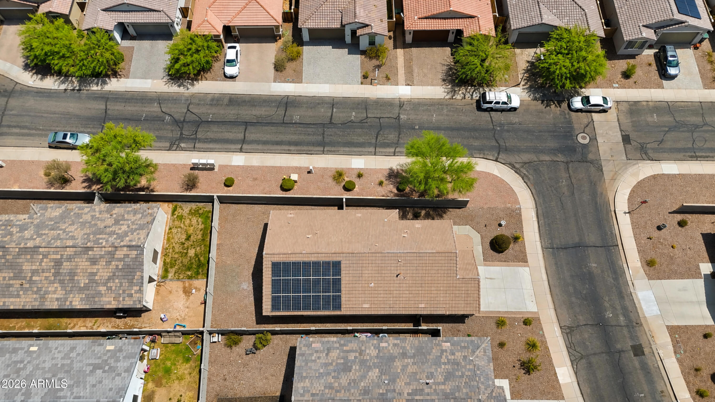 Aerial view of a tan tile-roofed home with rooftop solar panels and desert landscaping.