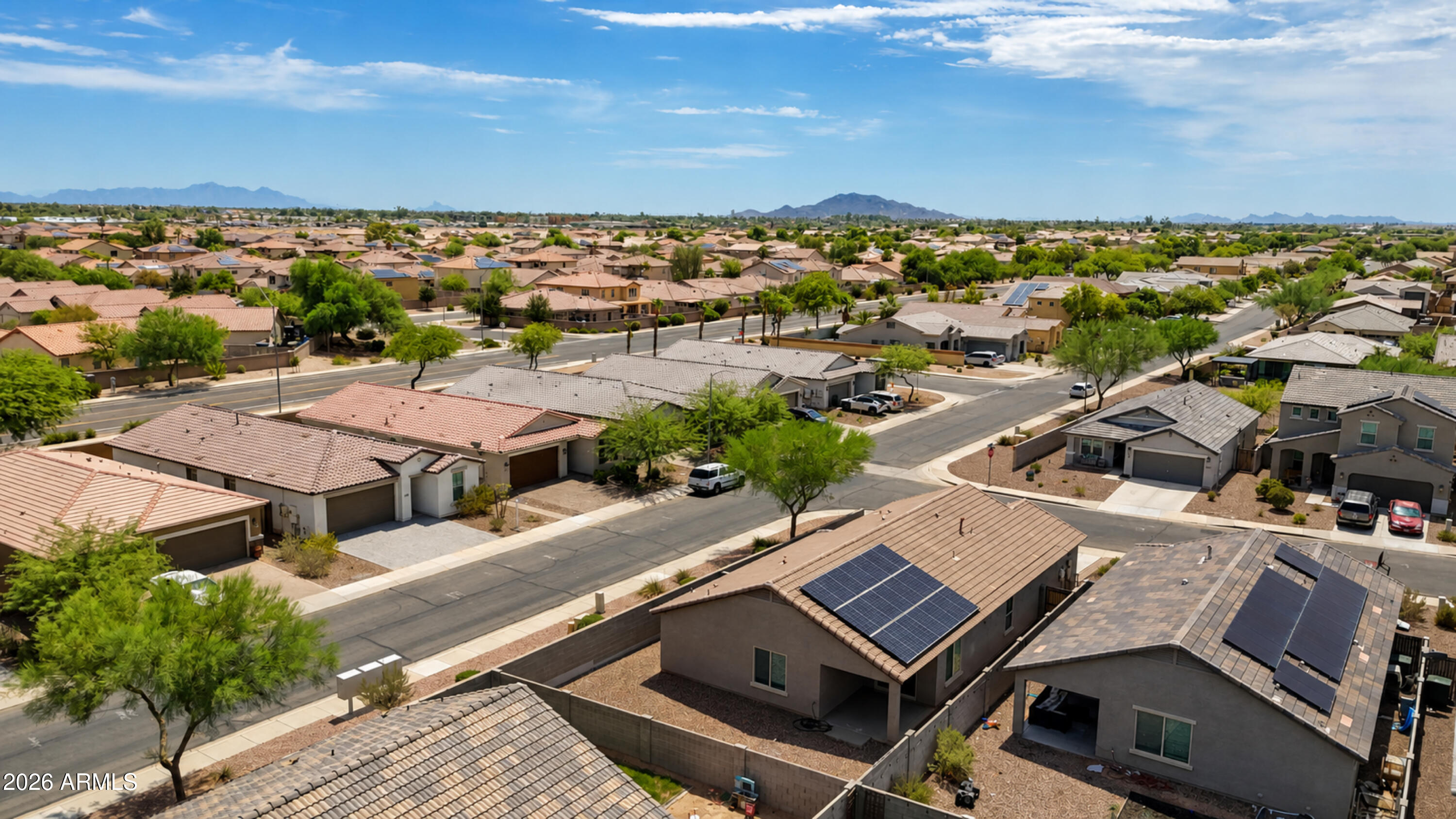 Aerial neighborhood view with solar panels on nearby homes and distant mountain ridges.