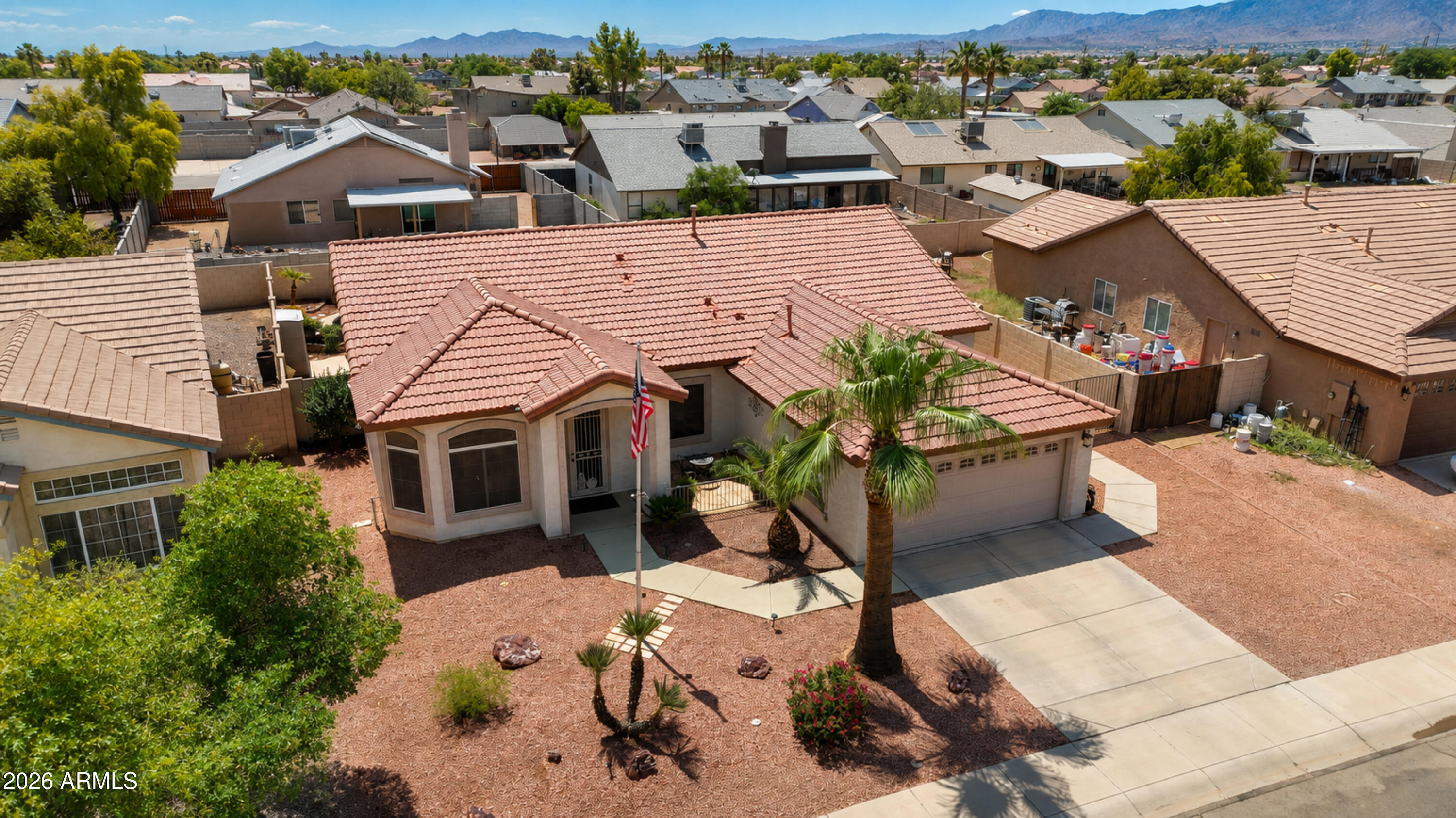 Aerial view of a stucco home with a red tile roof, palm trees, and desert landscaping.