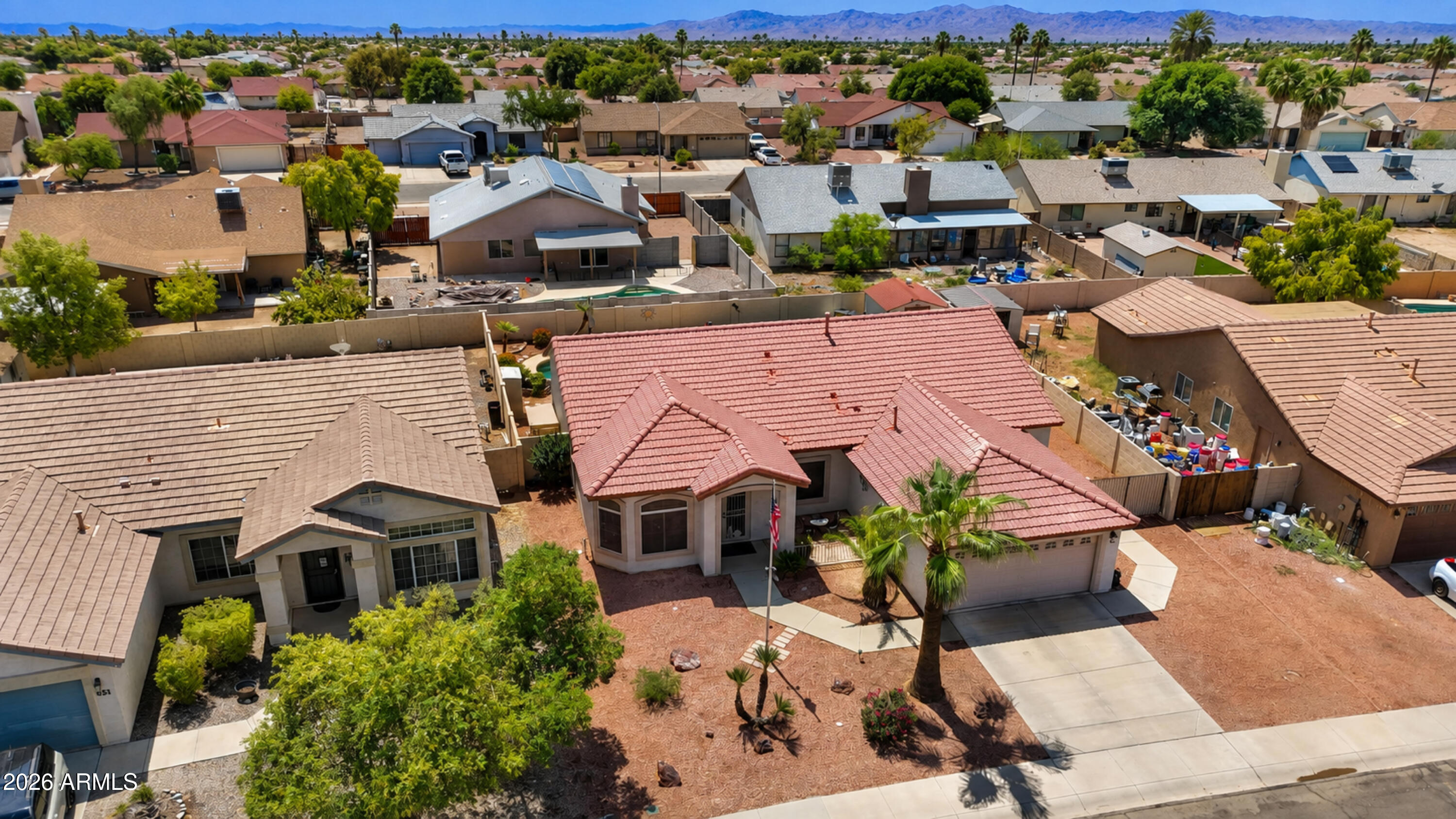 Aerial view of a red tile-roofed home with desert landscaping, palm trees, and distant mountains.