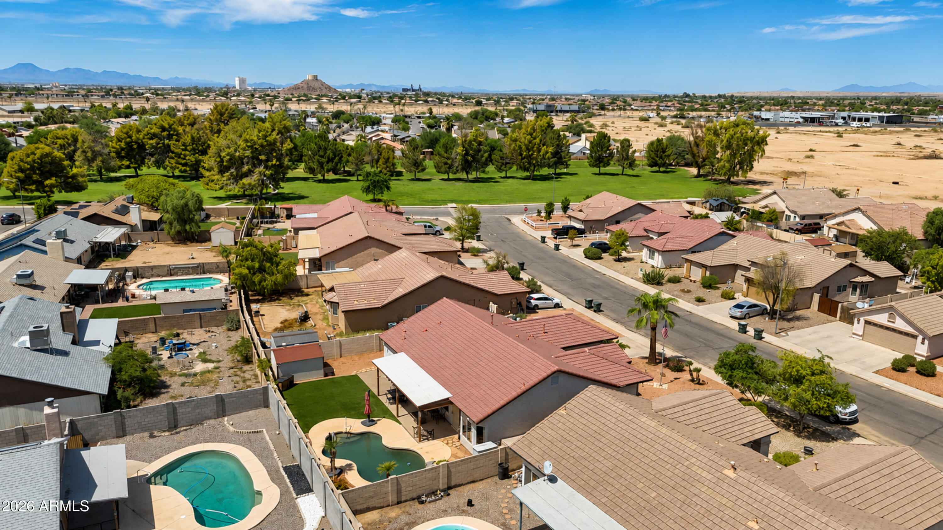 Aerial view of a Casa Grande home and neighborhood, with backyard pools, a green park, and distant mountains.