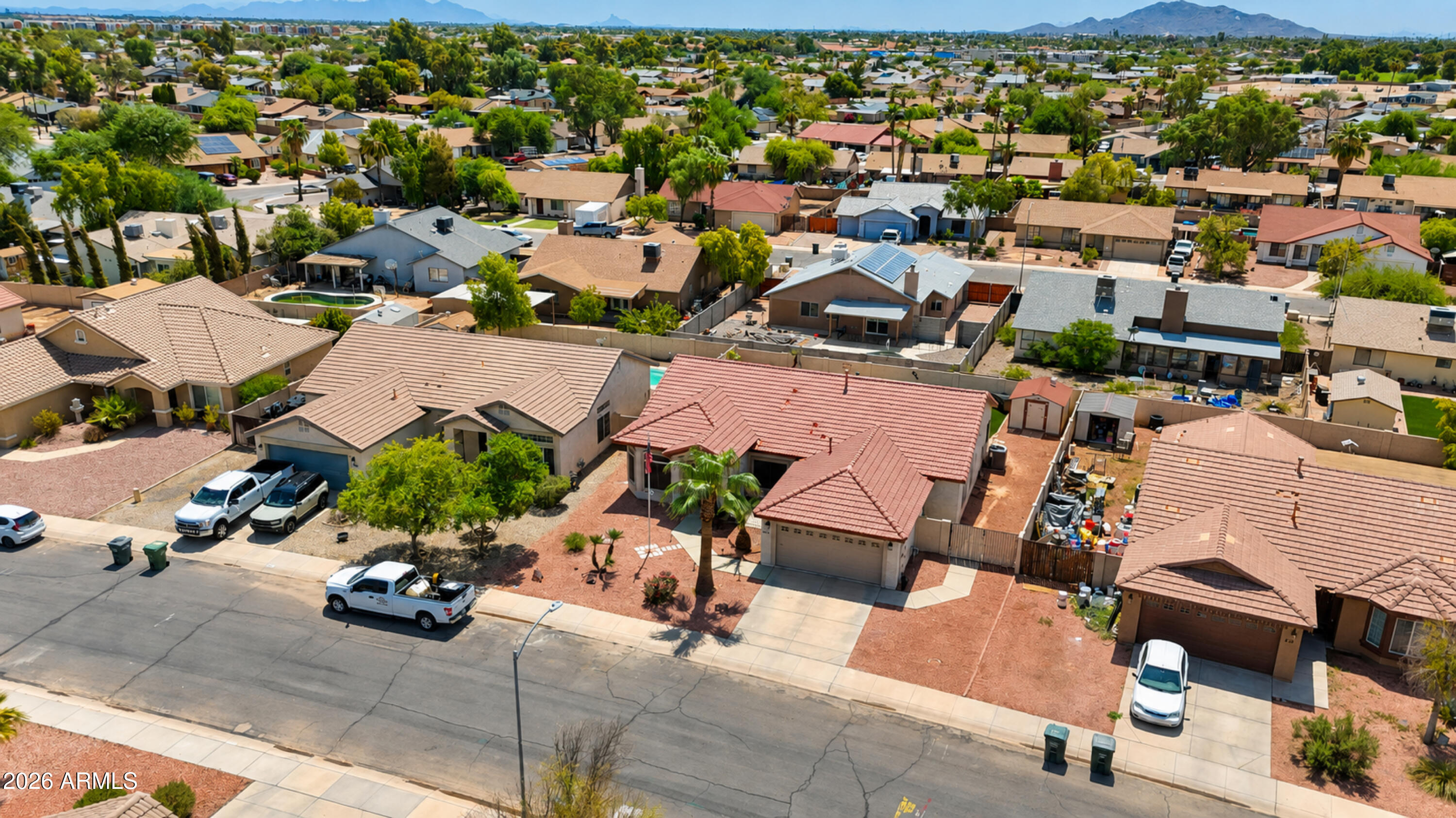 Aerial view of a red-tile-roof home among desert homes, with mountains in the distance.