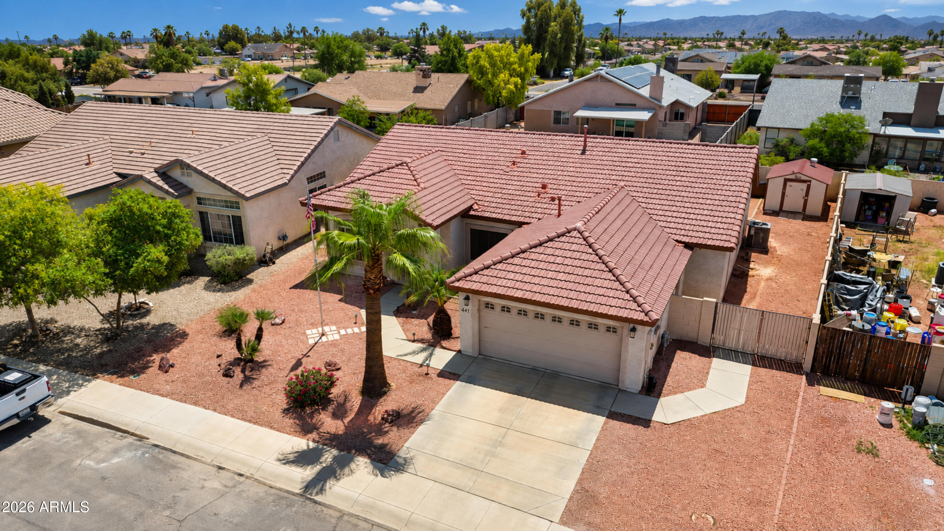 Aerial view of a red-tile-roof home with palm trees, gravel landscaping, and mountains in the distance.