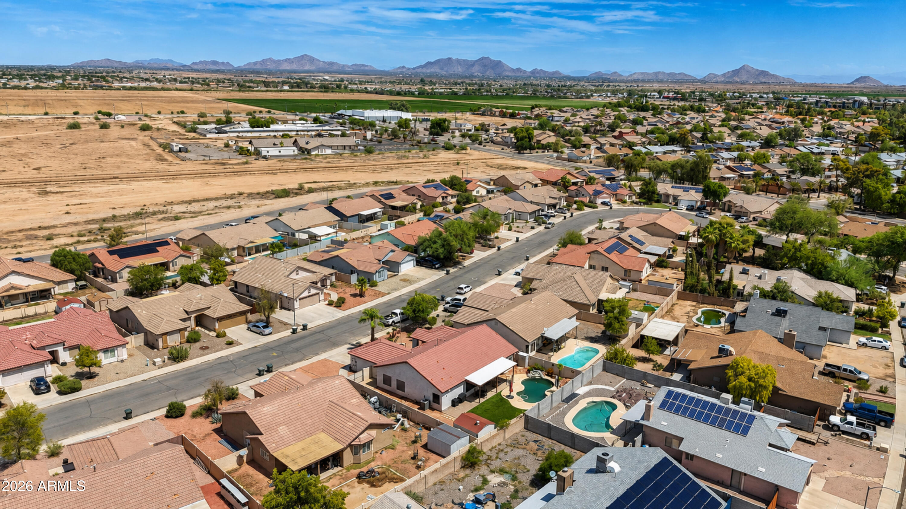 Aerial view of a residential neighborhood, with desert terrain and distant mountains on the horizon.