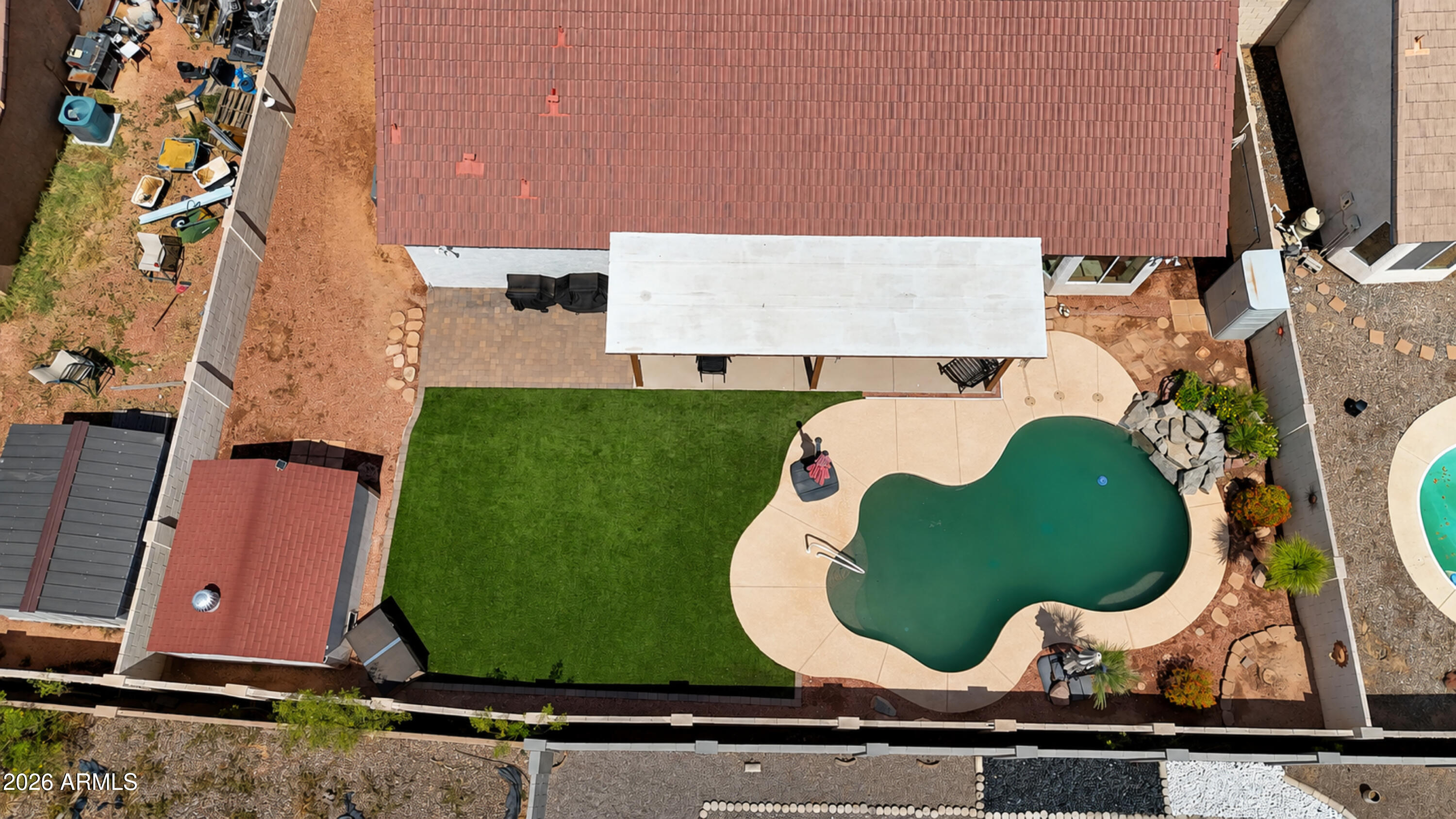 Aerial view of a backyard with a freeform pool, covered patio, and green lawn.