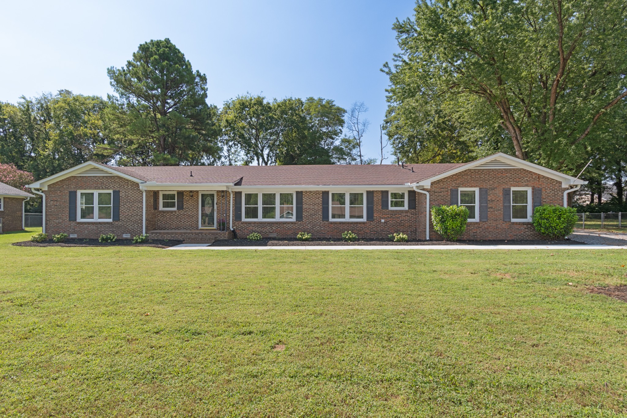 Single-story brick ranch home with dark shutters, landscaped beds, and a broad front lawn.