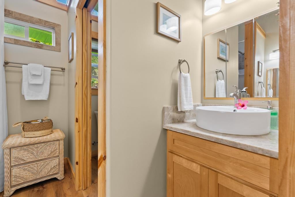 Bathroom with a white vessel sink, wood vanity, high windows, and wicker storage cabinet.