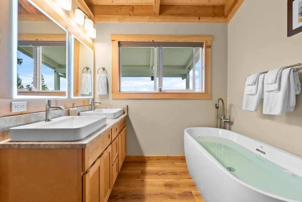 Bathroom with a double-sink wood vanity and freestanding soaking tub beneath a wood ceiling.