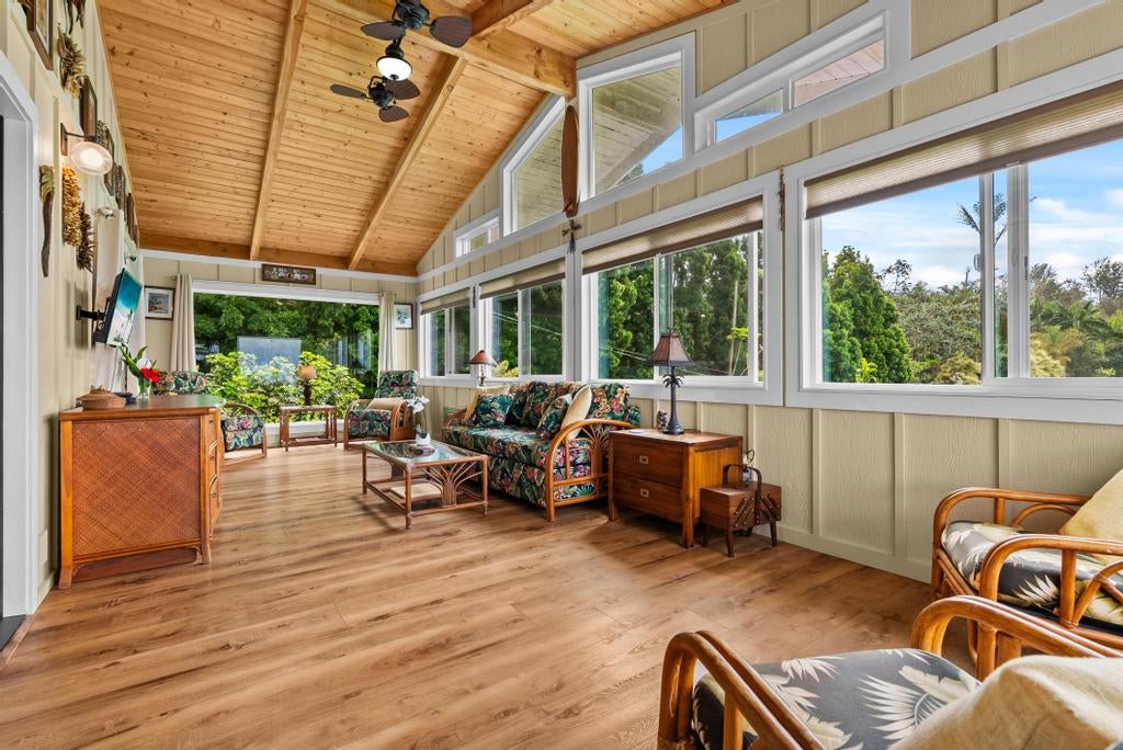 Furnished sunroom with a vaulted wood ceiling, floral seating, and large windows overlooking greenery.