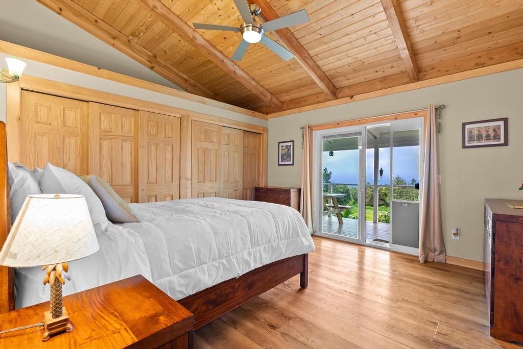 Bedroom with a vaulted wood ceiling, built-in closets, and sliding doors opening to an ocean view.