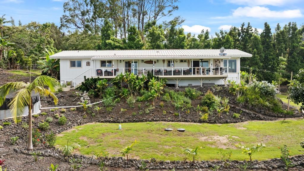 Long white home with a furnished covered veranda, tropical landscaping, and a broad front lawn.