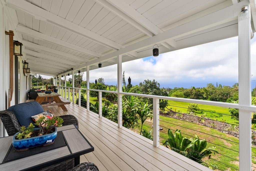 Covered porch with wicker seating and a wooden table overlooking a green garden.
