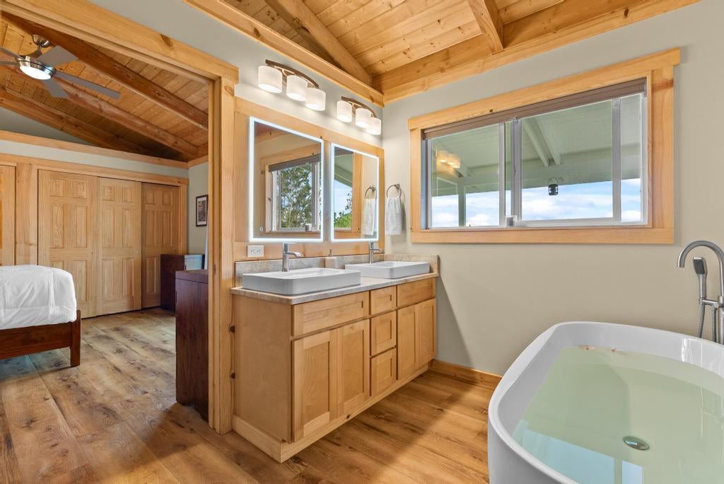 Bathroom with double-sink wood vanity, soaking tub, and vaulted wood ceiling.