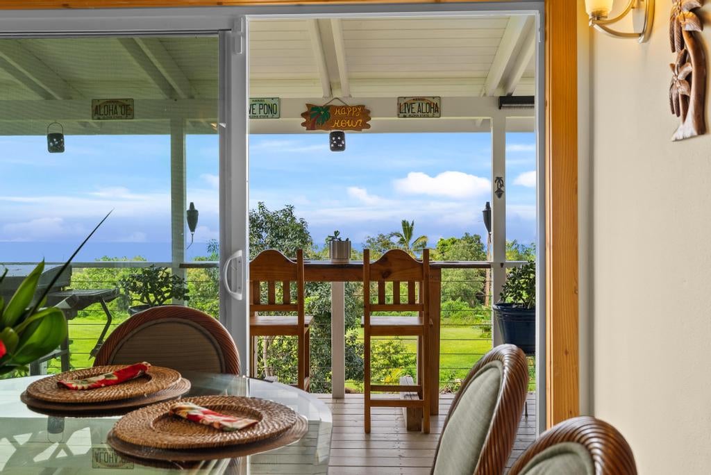 Dining area opening onto a covered lanai, with tropical greenery and ocean views beyond.