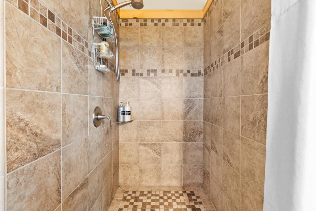 Walk-in shower with tan tiled walls, mosaic accents, and a checkerboard floor.